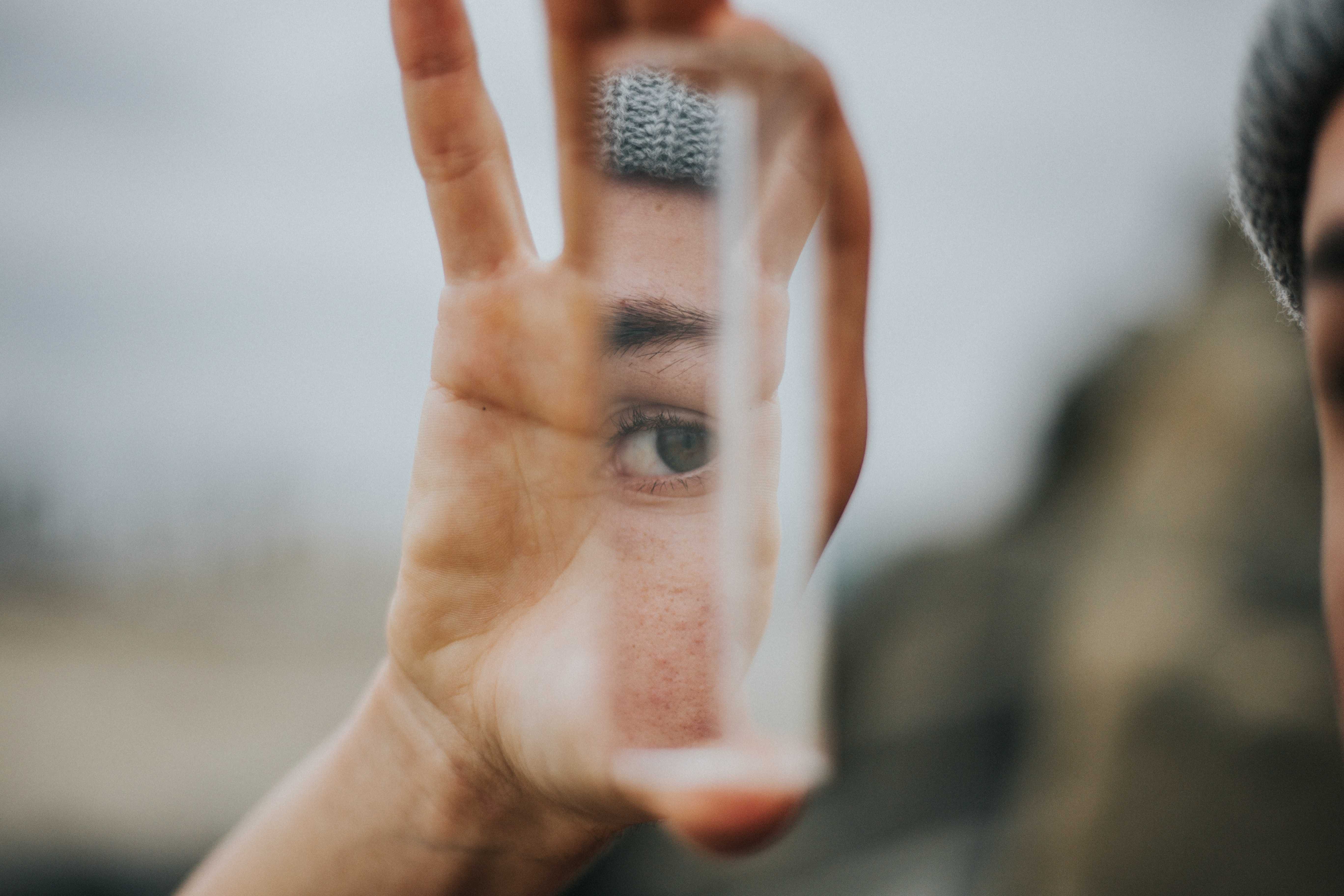 Eye reflected in a small piece of mirror held up by a person.