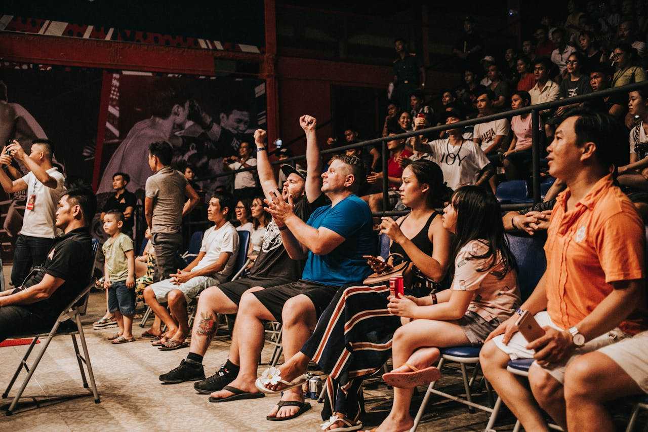 An image of an audience in foldable chairs, with people cheering and clapping.