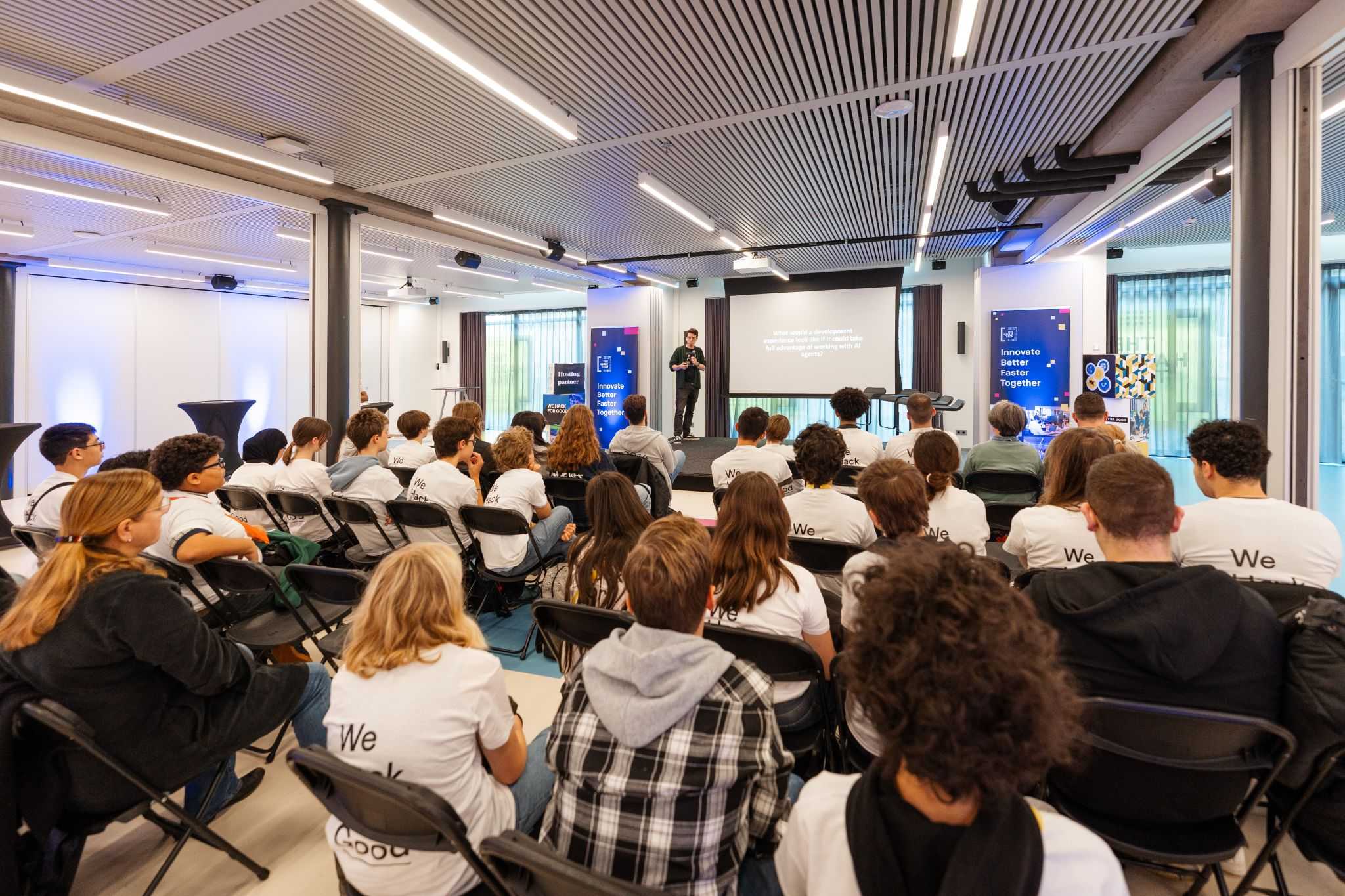 A photo of the event, a crowd of kids sitting in front of the stage where someone is giving a talk.